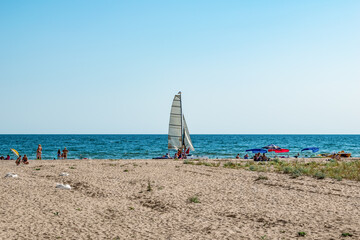 Few people on a wild beach in Zalizny Port (Kherson region, Ukraine). One sailboat amid green grass, white sand and turquoise-blue water