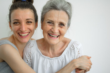 Happy senior mother is hugging her adult daughter, the women are laughing together, sincere family of different age generations having fun on white background, mothers day.