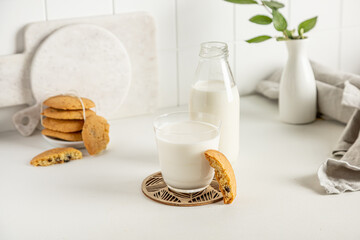 cookies and milk in a glass and bottle  on a white table with a napkin and little vase