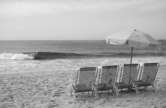 Monochrome image of group of empty chairs with umbrella on the sandy beach