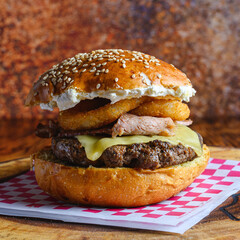 Closeup of a delicious beef burger with onion rings on a table with a blurry background