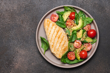 Grilled chicken breast with spinach salad, quinoa and tomatoes. Healthy food on dark background with copy space