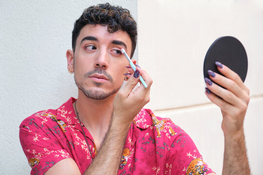 Young caucasian man with long false nails applying red eye shadow at street.