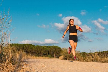 Front view of a caucasian young woman running and jumping in a mountain path during the golden hour.