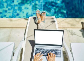 top view woman working on laptop computer with white blank screen, female hands typing keyboarding text, lying by the pool