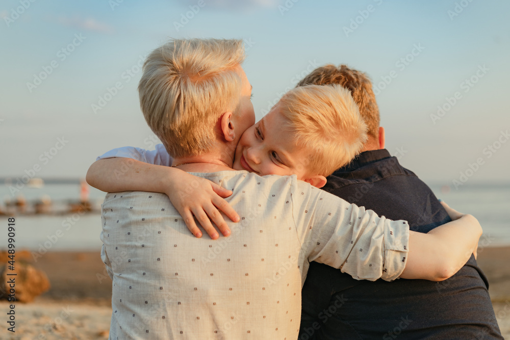 Wall mural portrait of loving caucasian family on sunset on beach. blond boy hugging mother