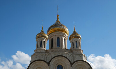 Fototapeta na wymiar Ancient and medieval golden Domes with golden crosses on the Orthodox Church against the blue sky with clouds. Exterior facade with white walls, white stone church.