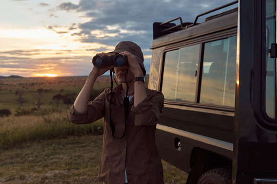 girl standing around a tourist car and looking through binoculars. Against the background of the sunset