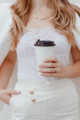 White paper disposable cup with hot drink in female hands weared in white suit.