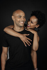 latin girl with afro hugging bald latin guy from behind. Couple on black background