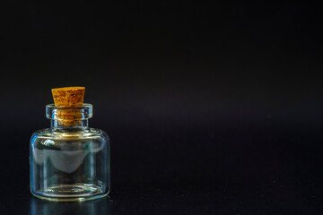 small glass jar with a cork on a black background