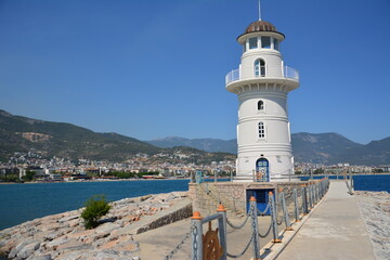 Fototapeta na wymiar white and blue lighthouse with concrete path on blue sea and town background, Alanya Turkey