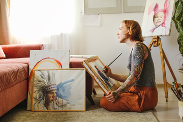 Creative red-haired girl hipster woman with paintings in home workshop, girl draws, creativity and...