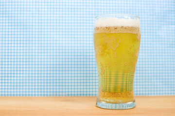 A glass of beer for Oktoberfest with a blue and white background on a wooden board
