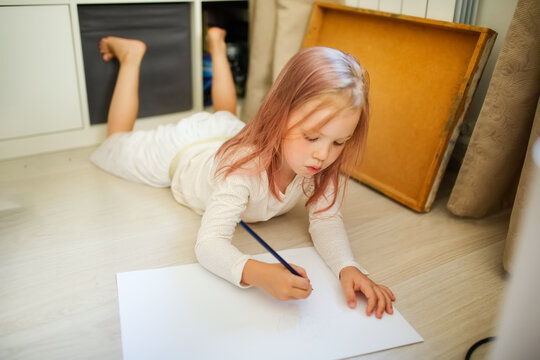 Funny european baby toddler draws on the floor of the house in a bright real room, lifestyle