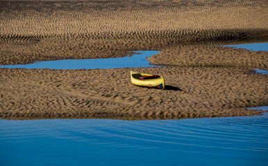 An abandoned yellow canoe lies on a sandbank in the late afternoon sun
