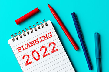 Planning 2022 concept. Notepad labeled Planning 2022  and multi-colored markers on turquoise background