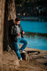 Young man in a leather jacket stands pensive and serious under a tree in autumn