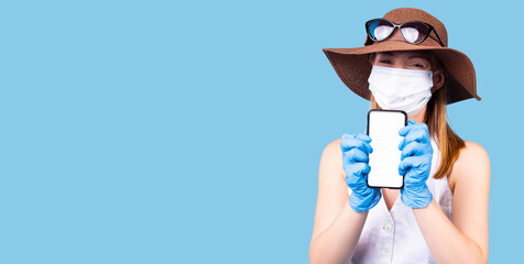 Satisfied woman wears protective medical mask not to infect other people, uses cell phone for surfing internet to find remedy.