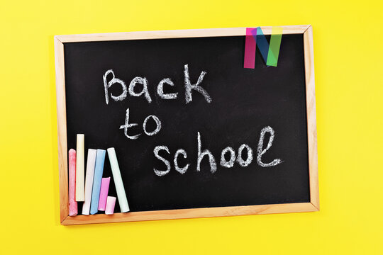 black chalk board with handwritten Back to school and school supplies chalk on yellow background top view