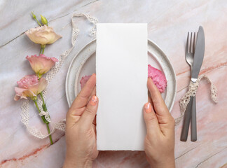 Hands holding wedding menu over a ceramic plate on a marble table