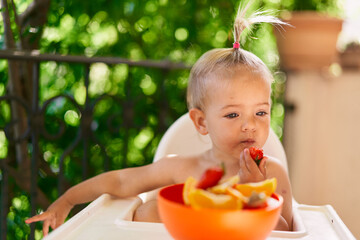 Little girl eats strawberries, lost in thought