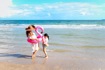 Naklejka premium Girl with parent wearing colorful inflatable swim ring running on summer beach, kids and mother on tropical sand beach, family spending time and having fun together on summer vacation.