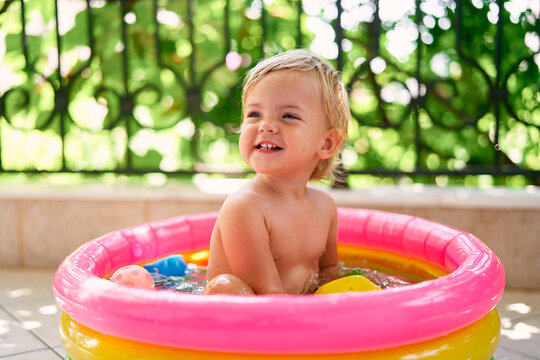 Little smiling baby sits in a small inflatable pool