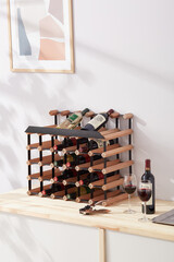 Interior photo: stylish wine rack with bottles is located on the table near wine glasses. Wine...