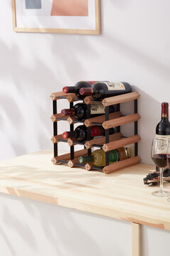 Interior photo: stylish wine rack with bottles is located on the table near wine glasses. Wine shelf is made of wood and metal and designed for 12 bottles. 