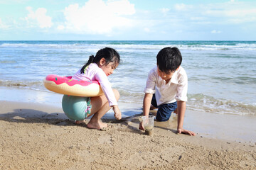 Two cute kids boy and girl having fun together on sandy summer beach with blue sea, happy childhood friend playing with sand on tropical beach, brother and sister spending time on family vacation.