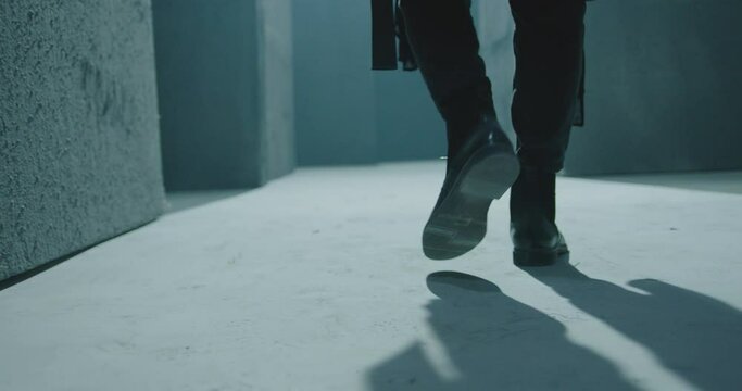 Close up of male legs in black boots.  Rear back view of man walking inside dark maze. Man walking inside dark room, corridor. Footage of mystical video. Shot on ARRI ALEXA Cinema Camera in slow motio