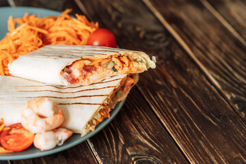 Shawarma cut in half with shrimps and tomato on wooden table