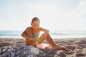 The child happily plays in the waves on the seashore
 A girl in a colorful swimsuit laughs while playing in the waves on the beach