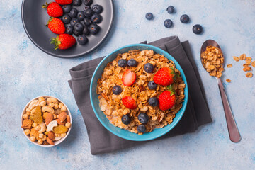 A bowl of healthy strawberry and blueberry cereal for a morning breakfast, with a plate of berries and a metal spoon. A meal to start the day right!