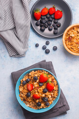 A bowl of healthy strawberry and blueberry cereal for a morning breakfast, with a plate of berries, a wooden bowl of ceral and a napkin. A meal to start the day right!