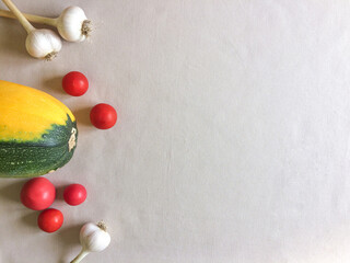 Green-yellow zucchini, heads of garlic and cherry tomatoes on beige background. Fresh vegetables contain vitamins and are good for health. Autumn. Space for text, flat lay. Harvest. Healthy food