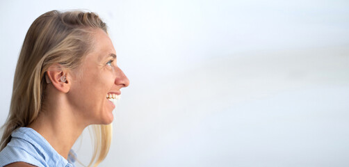 Woman's face in profile. Person wears beige colour hearing aid on ear. Problem with ear. Light...