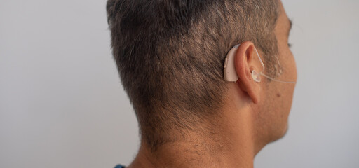 Obraz premium Man's head in profile, close-up. Person wears beige colour hearing aid on ear. Problem with ear. Light background. Technology to hear well. Equipment for communication.