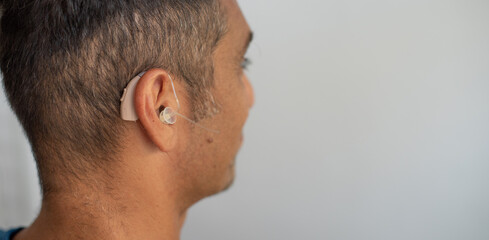 Obraz premium Man's face in profile. Person wears beige colour hearing aid on ear. Problem with ear. Light background, space for text. Technology to hear well. Device for communication.