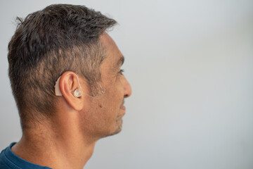 Man's face in profile. Person wears beige colour hearing aid on ear. Problem with ear. Light background, space for text. Technology to hear well. Device for communication.