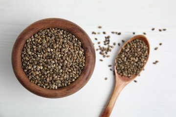 Wooden bowl and spoon with organic hemp seeds on white table, flat lay