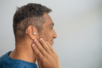 Fototapeta premium Man's face in profile. Person wears beige colour hearing aid on ear. Problem with ear. Light background, space for text. Technology to hear well. Equipment for communication