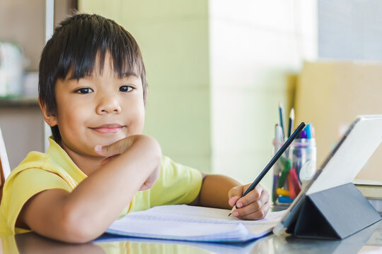 Portrait image of 7-8 years old kid. Happy Asian student child boy using and touching smart pad or tablet for do his homework and online learning (E-learning). Back to school, Study from home.