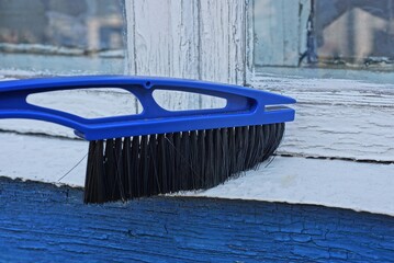 plastic blue brush with black bristles sweeps the dust off the white windowsill on the street