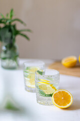 Homemade refreshing summer lemonade drink with lemon slices and ice in glasses with flowers bouquet in a vase on the background