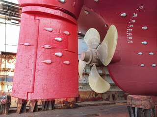 The stern of a large ship with a copper propeller, with a steering gear on a slipway in a dry dock....