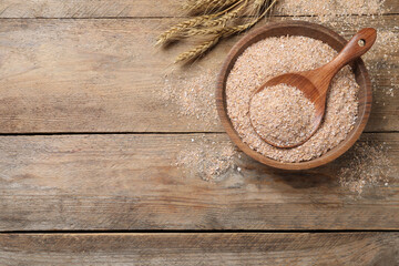 Wheat bran and spoon in bowl on wooden table, flat lay. Space for text