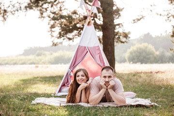 Relaxed young couple sitting near wigwam in park on sunny day. summer holiday vacation. man and woman are hugging outdoors and huving fun. © Andriy Medvediuk