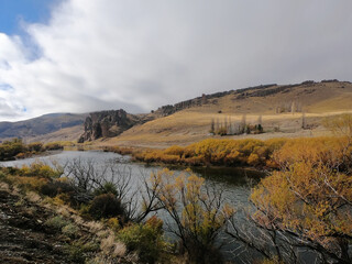 Idyllic alpine landscape. View of the river flowing across the golden valley and mountains. The pure water stream, yellow grassland, hills and rock formation in autumn.